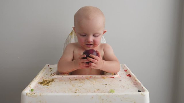 Cute baby girl soiled in food while eating plum.