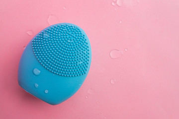 Blue facial cleansing brush on pink background. Beauty and skincare concept. Brush for face...