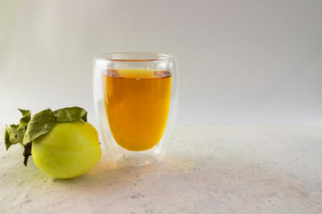double-walled glass of apple juice and apple lies nearby