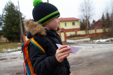 Little European boy holding a paper boat in his hand. The child wants to launch a boat to swim in the stream in the spring.