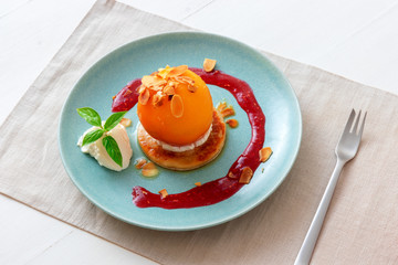 Roasted peaches with lemon, lime and basil creme fraiche and raspberry coulis. Tasty sweet fruit dessert ala Gordon Ramsey. White wooden table background.