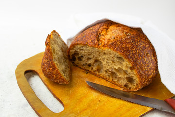 Freshly baked cereal bread on a wooden board under a white towel.