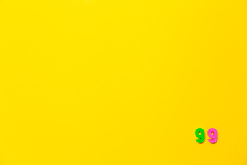 A green and pink plastic toy number ninety-nine is located in the lower right corner on a yellow background