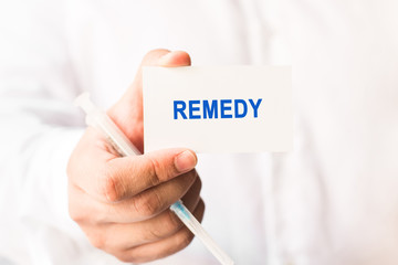 Word remedy on a white background with a syringe in hand. Medicine concept