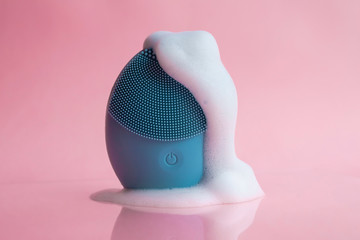 Silicone brush for washing face in foam. Blue facial cleansing brush on pink background. Beauty and...