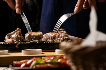 sirloin steak on a very hot stone being cooked by a man to his own taste on a wooden table with a knife and fork