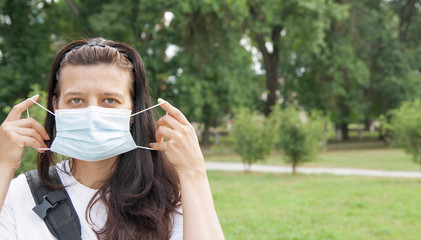 Middle aged woman straightens a medical mask outdoors with a copy space. New reality concept, virus protection.