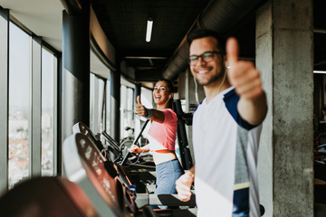 Young fit man and woman running on treadmill in modern fitness gym.