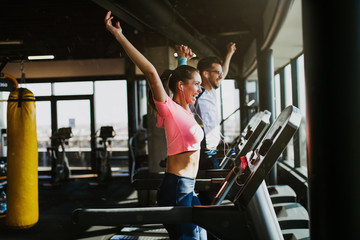 Young fit man and woman running on treadmill in modern fitness gym.