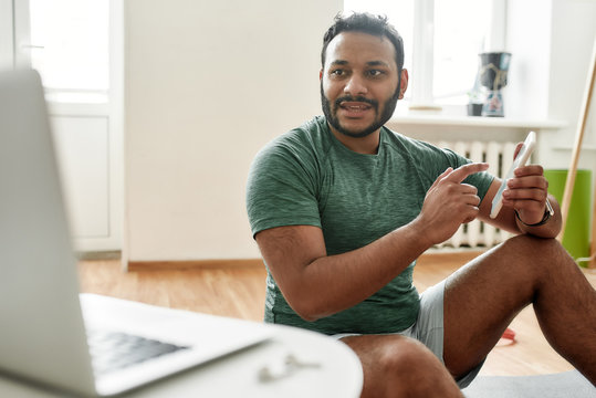 The best application. Young active man advertising smartphone app while streaming, broadcasting video lesson on training at home using laptop. Online personal trainer