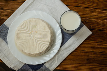 A glass of goat milk and a head of goat milk cheese stand on a wooden table. Cheese at home.