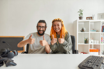 Cheerful man and woman showing thumbs up at camera. Young male and female technology blogger...