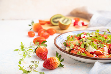 Vegetarian fruits and vegetables salad of strawberry, kiwi, tomatoes, microgreen sprouts on white concrete background. Side view, selective focus.