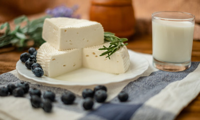 A glass of goat milk and a head of goat milk cheese stand on a wooden table. Cheese at home.