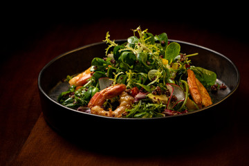 Shrimps salad with cherry tomatoes, cucumeber, avocado, lettuce and pomegranate on dish. Healthy seafood concept. Tasty grilled prawn shrimp and mix vegetable salad on black wood
