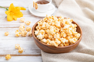 Popcorn with caramel in wooden bowl and a cup of coffee on a white wooden background. Side view.