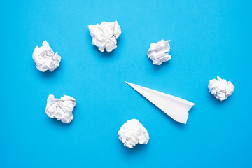 Obraz premium Paper plane and paper crumpled ball on the blue flat lay background.