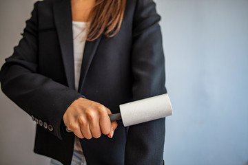 Woman with adhesive roller cleaning clothes. Woman cleaning black jacket with lint roller on light...