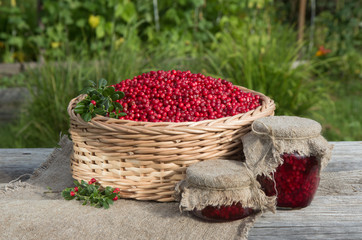 Fototapeta na wymiar Lingonberry jam in glass lars on the background of a basket with fresh berries.