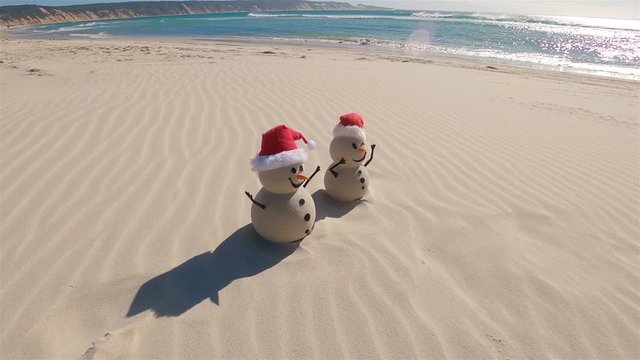 Two Sandy Christmas Snowmen are celebrating Christmas on a beautiful beach, zoom out
