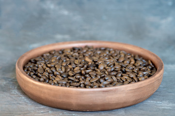Coffee beans close-up in a clay pan on a vintage background.