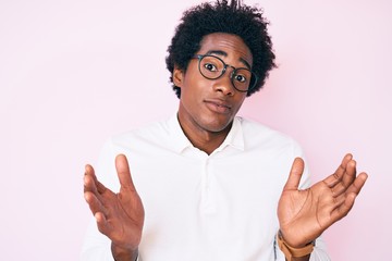 Handsome african american man with afro hair wearing business shirt and glasses clueless and confused with open arms, no idea and doubtful face.