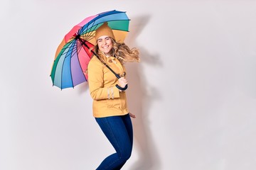 Young beautiful woman wearing winter clothes smiling happy. Jumping with smile on face holding colorful umbrella over isolated white background