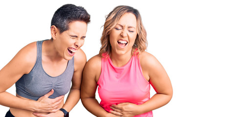 Couple of women wearing sportswear smiling and laughing hard out loud because funny crazy joke with hands on body.