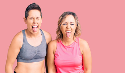 Couple of women wearing sportswear sticking tongue out happy with funny expression. emotion concept.