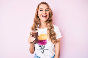 Young caucasian woman with blond hair drinking chocolate milkshake looking positive and happy standing and smiling with a confident smile showing teeth