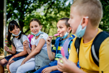 Group of children eating ice cream  outside. They are wearing a protective face mask down.