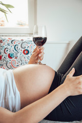 Pregnant woman holding glass of wine on her belly.