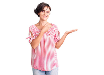 Beautiful young woman with short hair wearing casual summer clothes amazed and smiling to the camera while presenting with hand and pointing with finger.