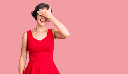 Beautiful young woman with short hair wearing casual style with sleeveless shirt smiling and laughing with hand on face covering eyes for surprise. blind concept.