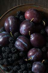 Plums and blackberries in a bowl, slice, selective focus and blur.