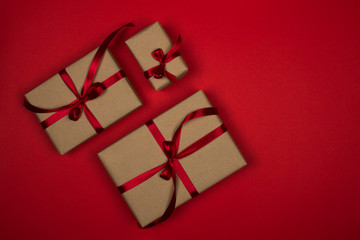 Gift box on a red background. Satin burgundy ribbon, bow, box wrapped in craft paper. Luxury gift, place for text. Holidays concept. View from above, layout for design. Concert of holiday shopping.