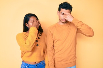 Beautiful latin young couple wearing casual clothes together tired rubbing nose and eyes feeling...