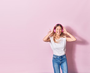 Obraz na płótnie Canvas Young beautiful blonde woman smiling happy. Jumping with smile on face listening to music using pink headphones over isolated background