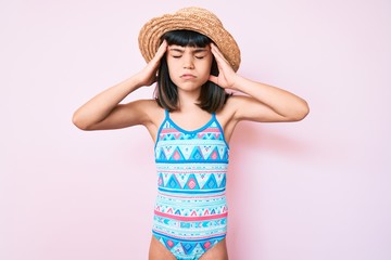 Young little girl with bang wearing swimsuit and summer hat with hand on head, headache because stress. suffering migraine.