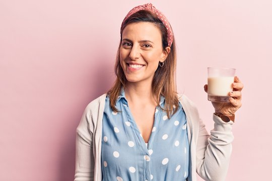 Young beautiful woman holding glass of milk looking positive and happy standing and smiling with a confident smile showing teeth