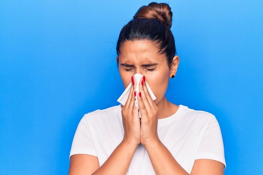 Young latin woman illness using paper handkerchief on nose. Standing over isoltated blue background