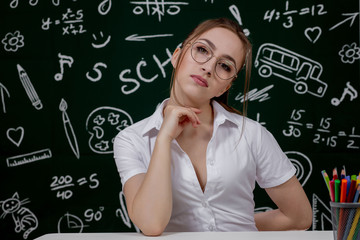 Fototapeta premium Young teacher is sitting near blackboard in classroom