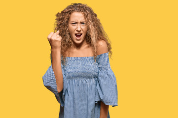 Beautiful caucasian teenager girl wearing summer dress angry and mad raising fist frustrated and furious while shouting with anger. rage and aggressive concept.