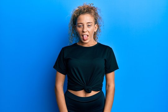 Beautiful caucasian teenager girl wearing black sportswear sticking tongue out happy with funny expression. emotion concept.