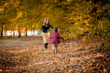 Happy young mother playing and having fun with her little baby son on sunshine warm autumn day in the park. Happy family concept