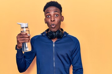 Young african american man wearing sportswear holding water bottle scared and amazed with open mouth for surprise, disbelief face