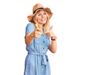 Obraz na płótnie Canvas Young beautiful blonde woman wearing summer hat and dress pointing fingers to camera with happy and funny face. good energy and vibes.