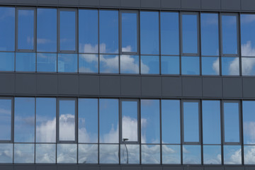 Close-up of a modern steel glass facade of a business building, with mirror reflection of the blue sky with some small clouds