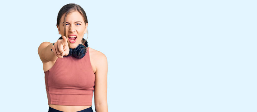 Beautiful caucasian young woman wearing gym clothes and using headphones pointing displeased and frustrated to the camera, angry and furious with you