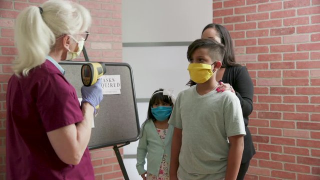 Due to mandates surrounding COVID19 pandemic a mother and her children get their temperature checked by a nurse before they proceed to the doctor for a routine checkup.